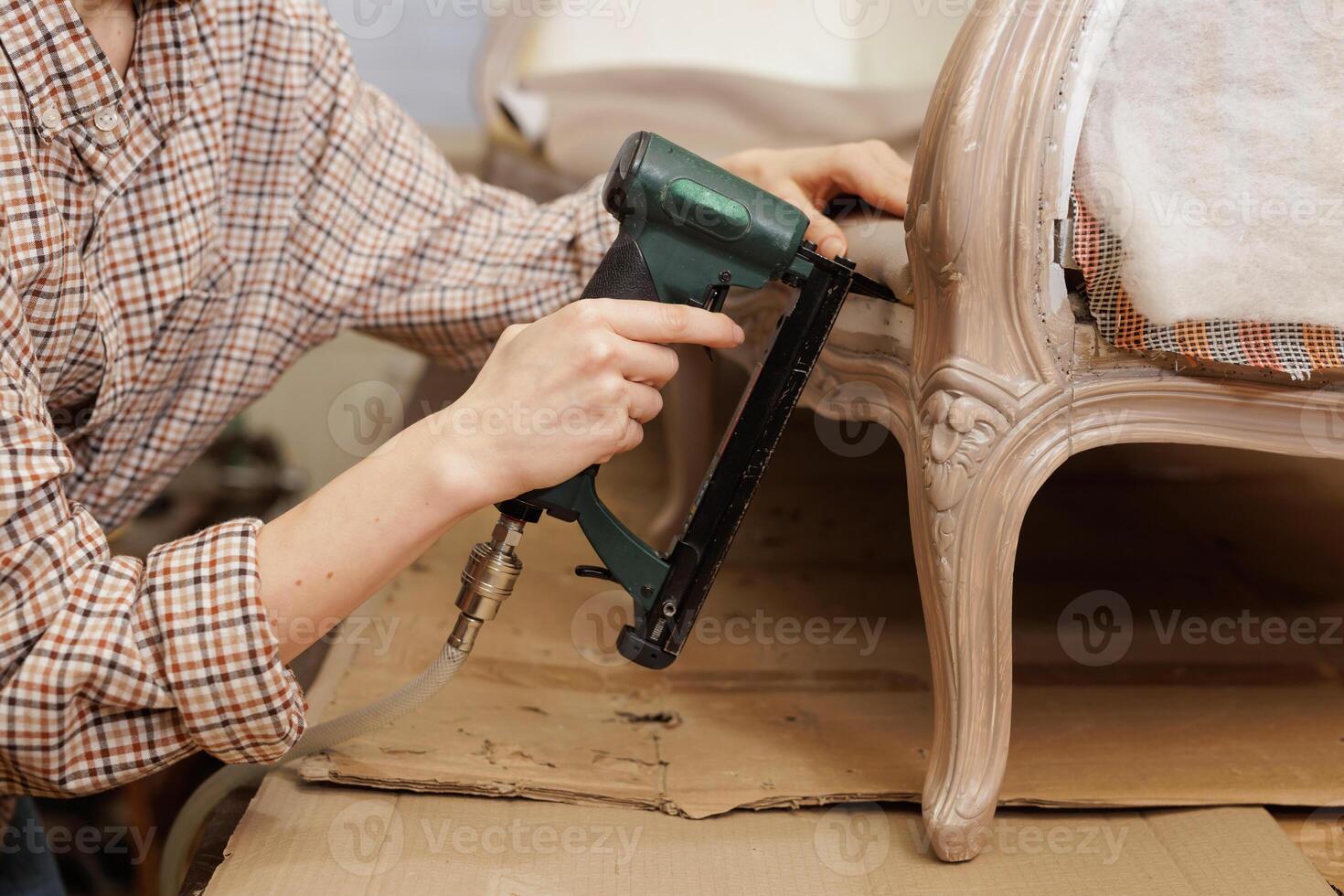Making new upholstery on old restored furniture. A woman works with a pneumatic stapler in her workshop. Furniture repair photo