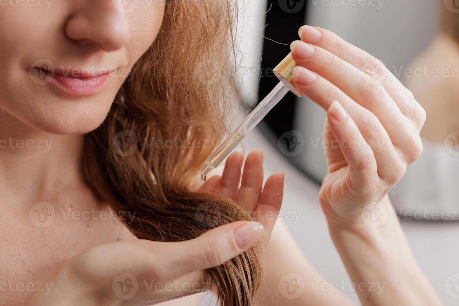 Cropped of blonde woman applying hair oil on ends while styling her beautiful hair at bathroom after morning shower, enjoying new hair care product, closeup shot photo