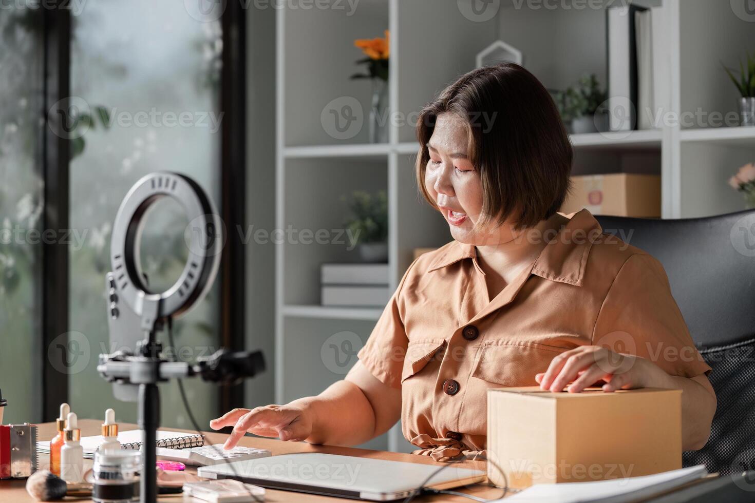 Young woman engaging her audience while livestreaming beauty cream sales from a modern home office photo