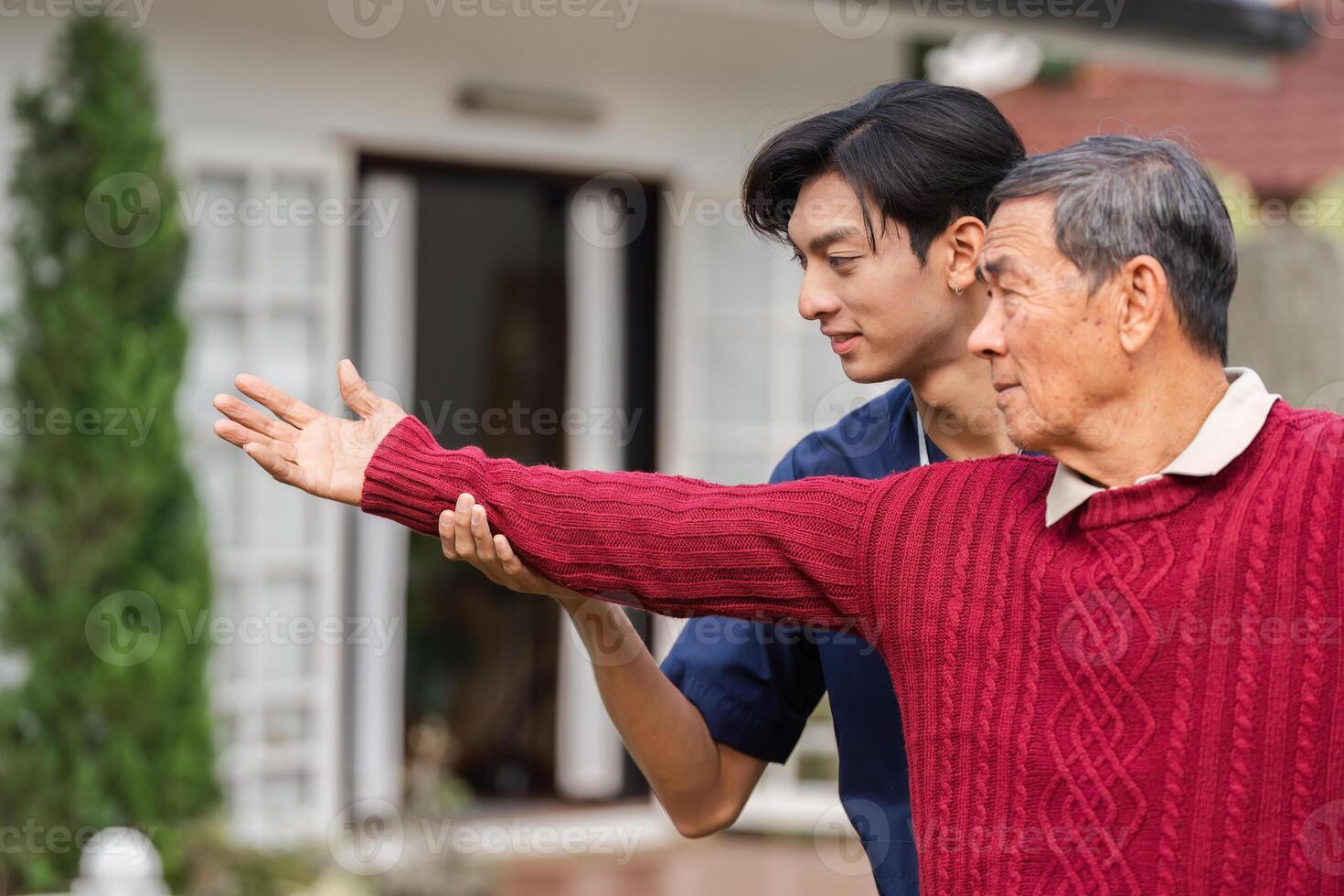 Young caregiver assisting elderly man with outstretched arm gesture in home garden photo
