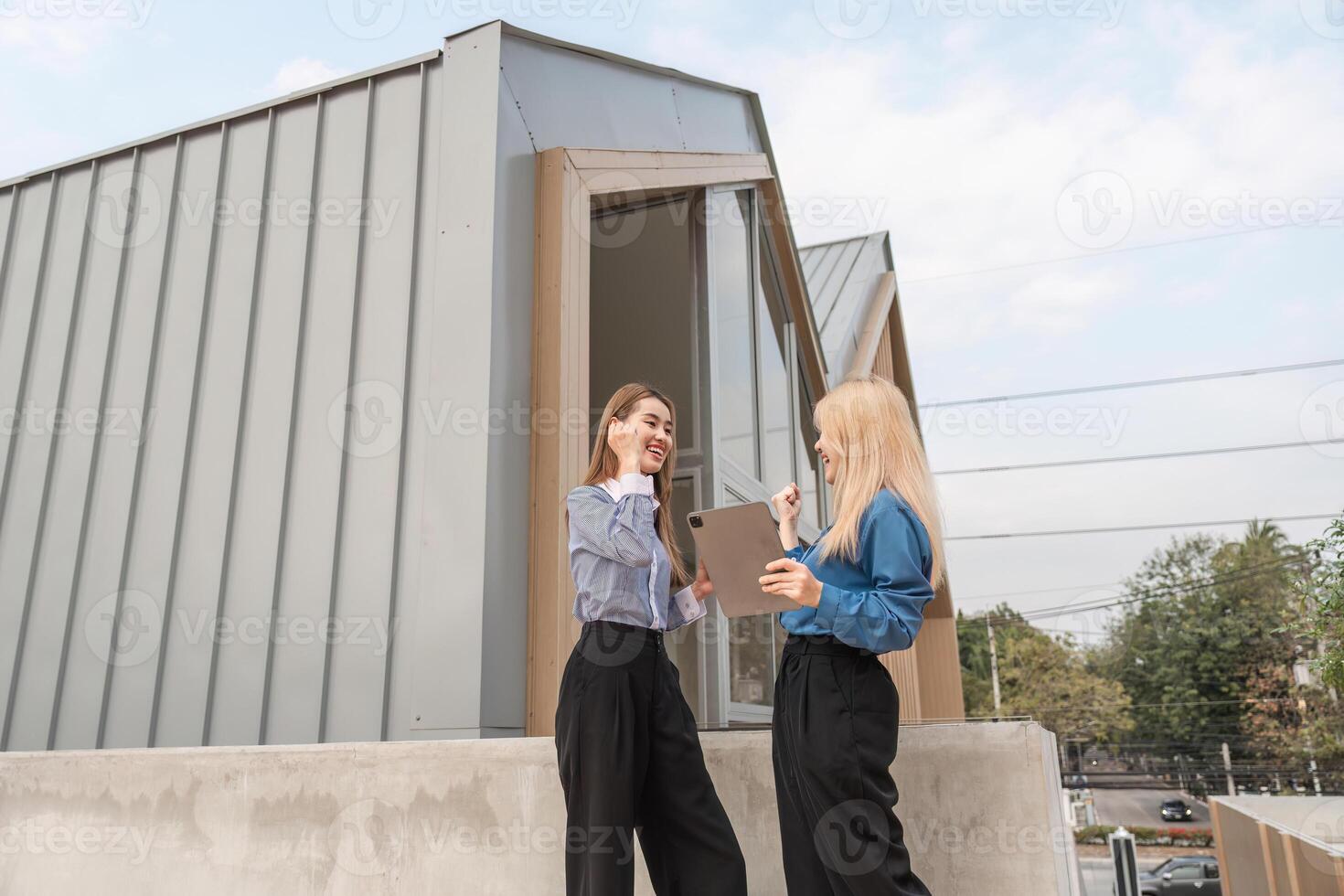 Diverse women discussing ideas enthusiastically with a tablet outdoors in a modern setting. photo
