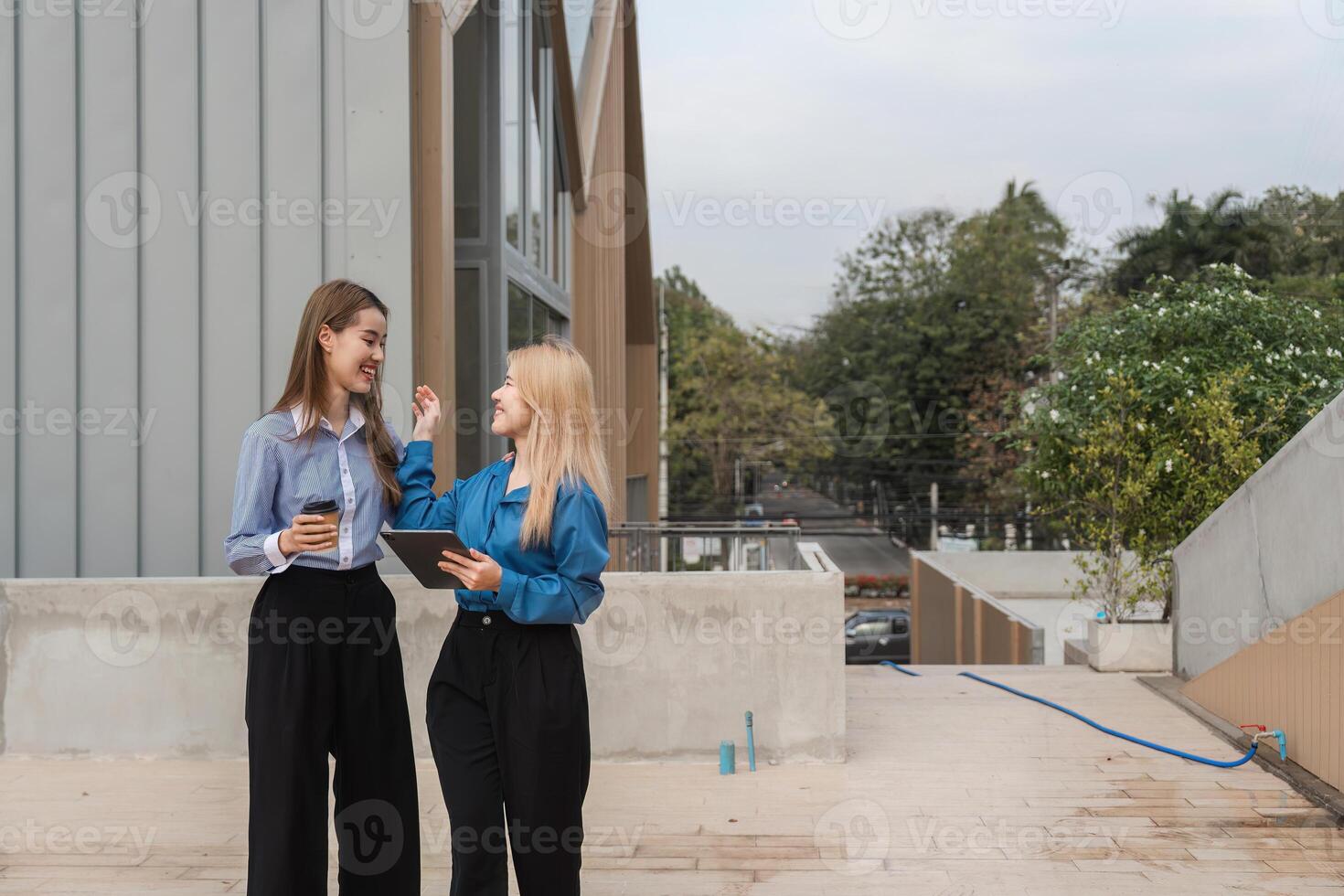 Diverse women enjoying conversation with a tablet and coffee outdoors in a modern environment. photo