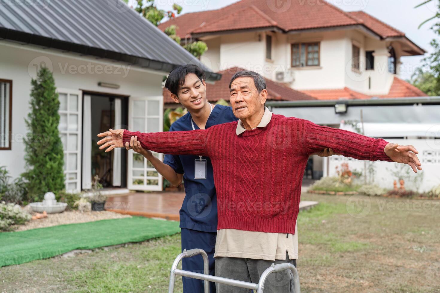Nurse encouraging elderly man to stretch arms while using walker in a supportive garden environment photo
