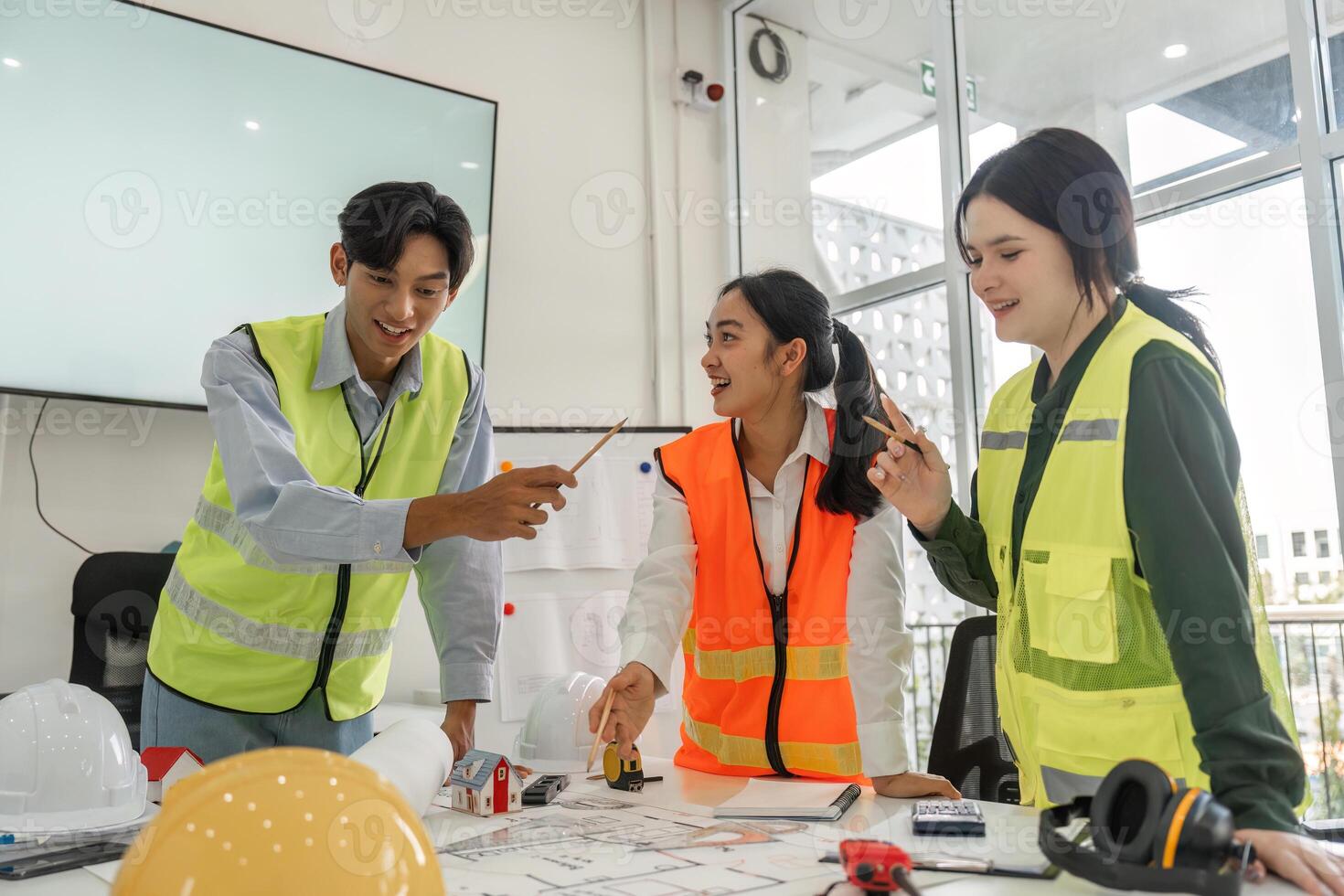 Joyful construction team engaging in brainstorming session with project plans and safety gear in a modern office photo