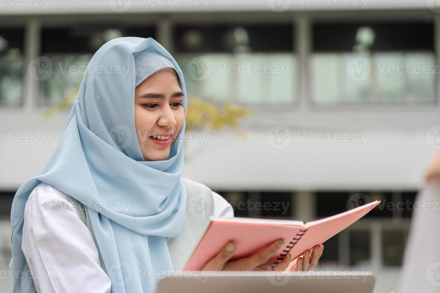 Young Muslim woman studying with notebook outdoors in a university setting. photo