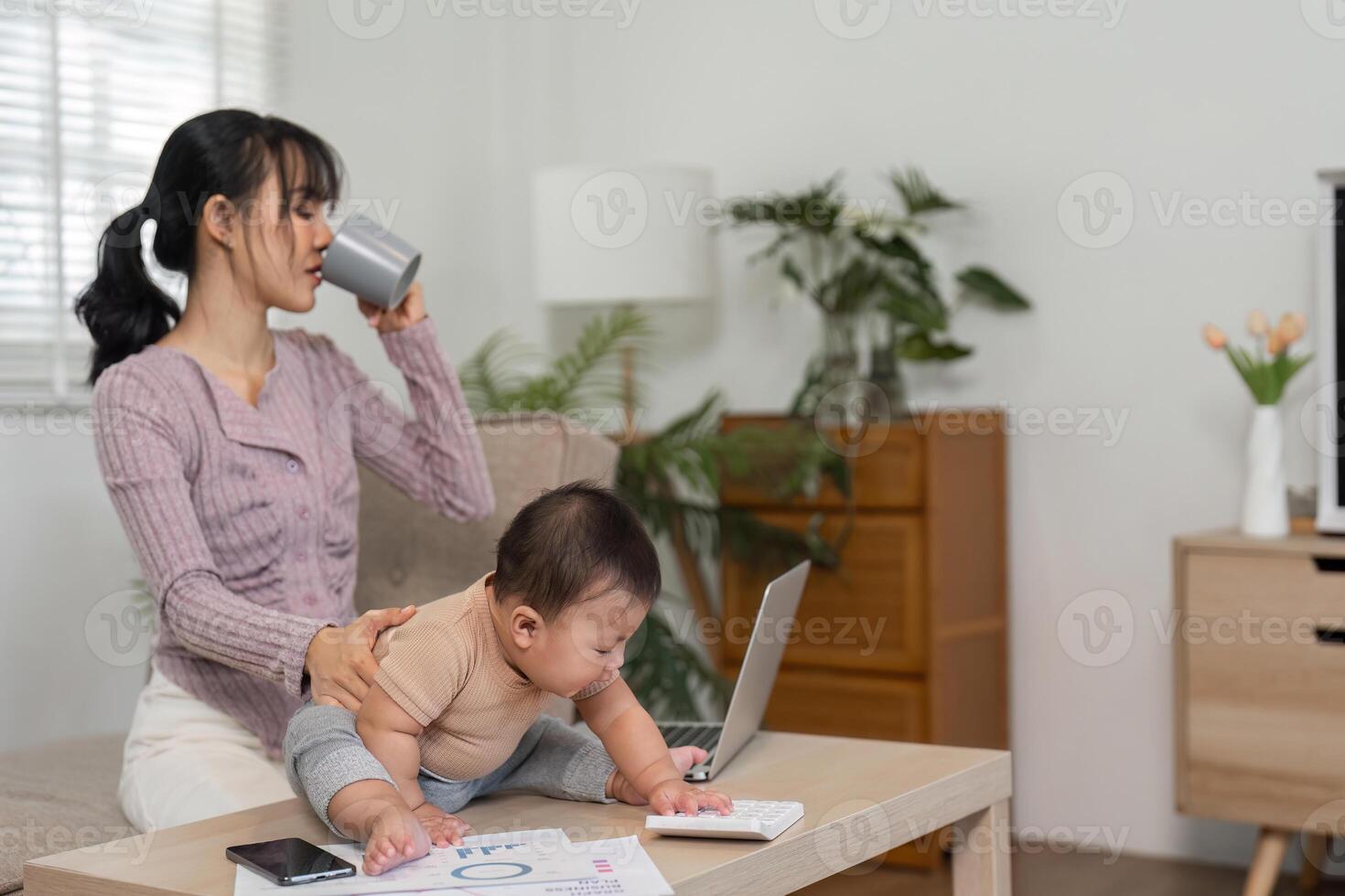 Mother sipping coffee while supervising her baby exploring a desk. photo