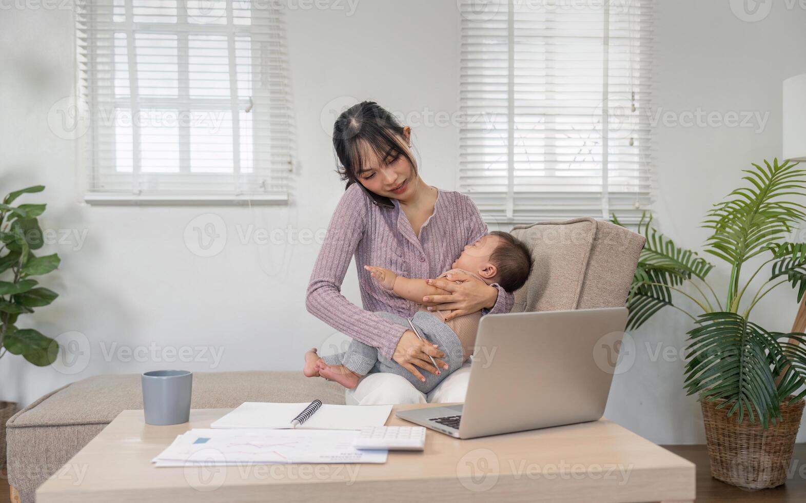 Mother multitasking on the phone while holding her baby in a cozy home office. photo