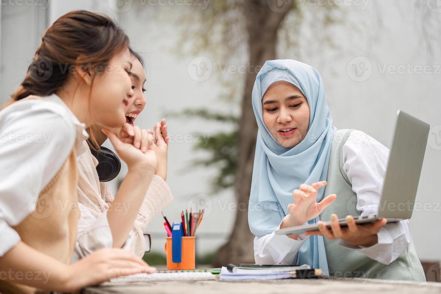 Diverse female students engaged in a group study session with a laptop outdoors. photo