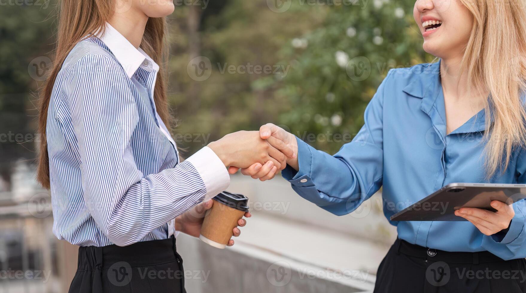Two businesswomen shaking hands outdoors, celebrating a successful collaboration. photo