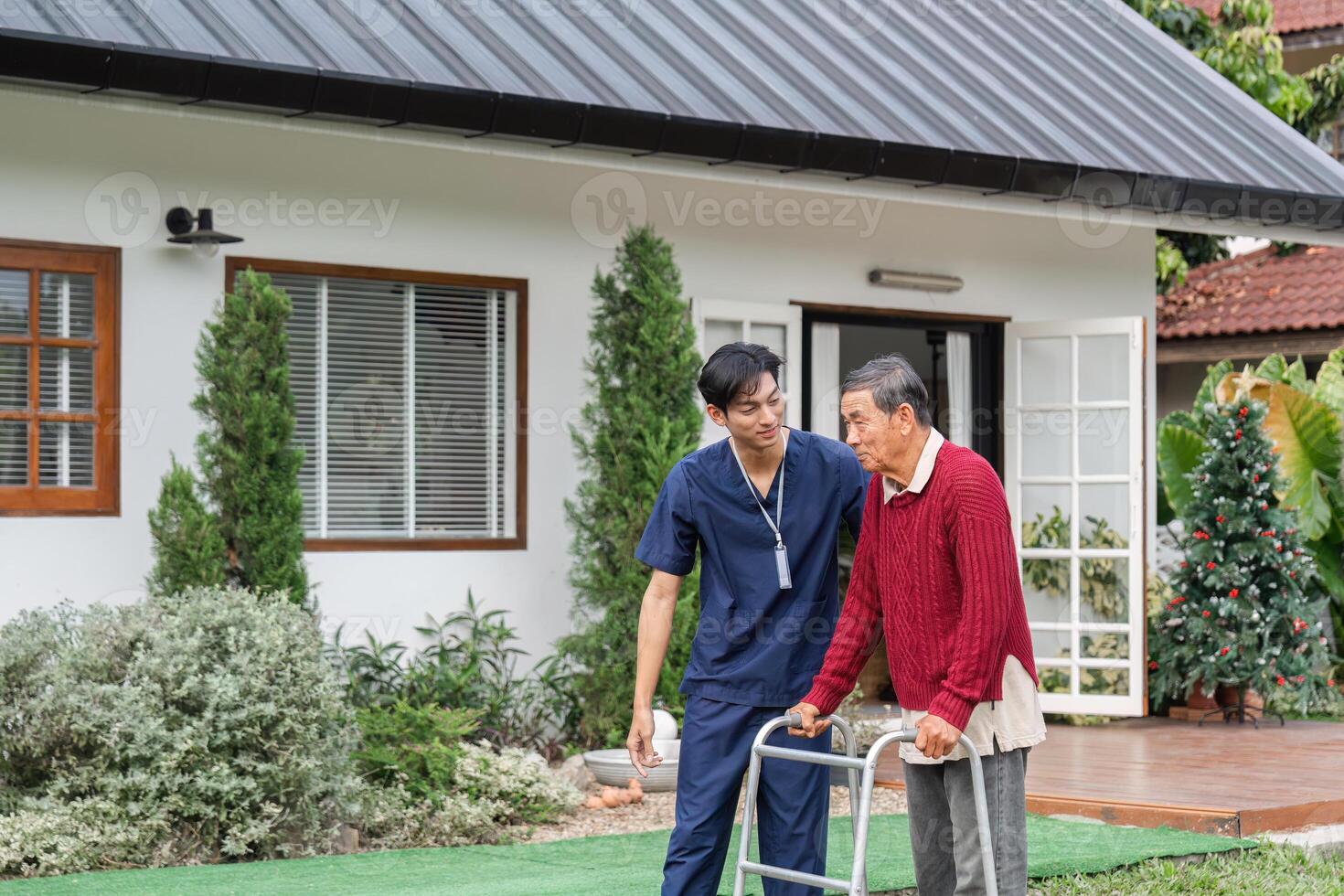 Nurse assisting elderly man with walker in a serene garden setting near a cozy home photo