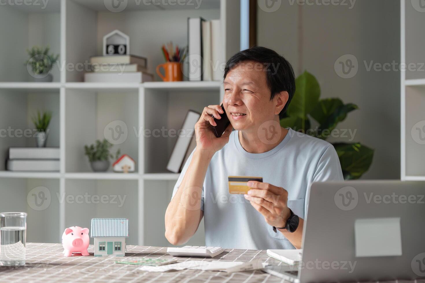 Smiling man using smartphone and credit card for online shopping while talking on the phone photo