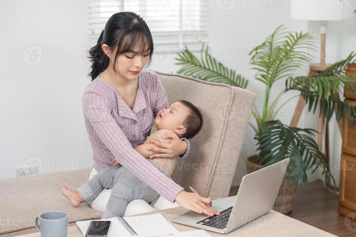 Working mother multitasking with baby on her lap while managing tasks from home office photo