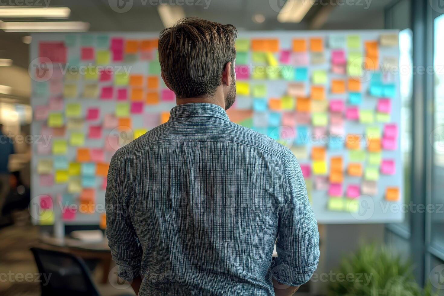 a man look to sticky notes on a task board to organize ideas and workflow in a office.. photo