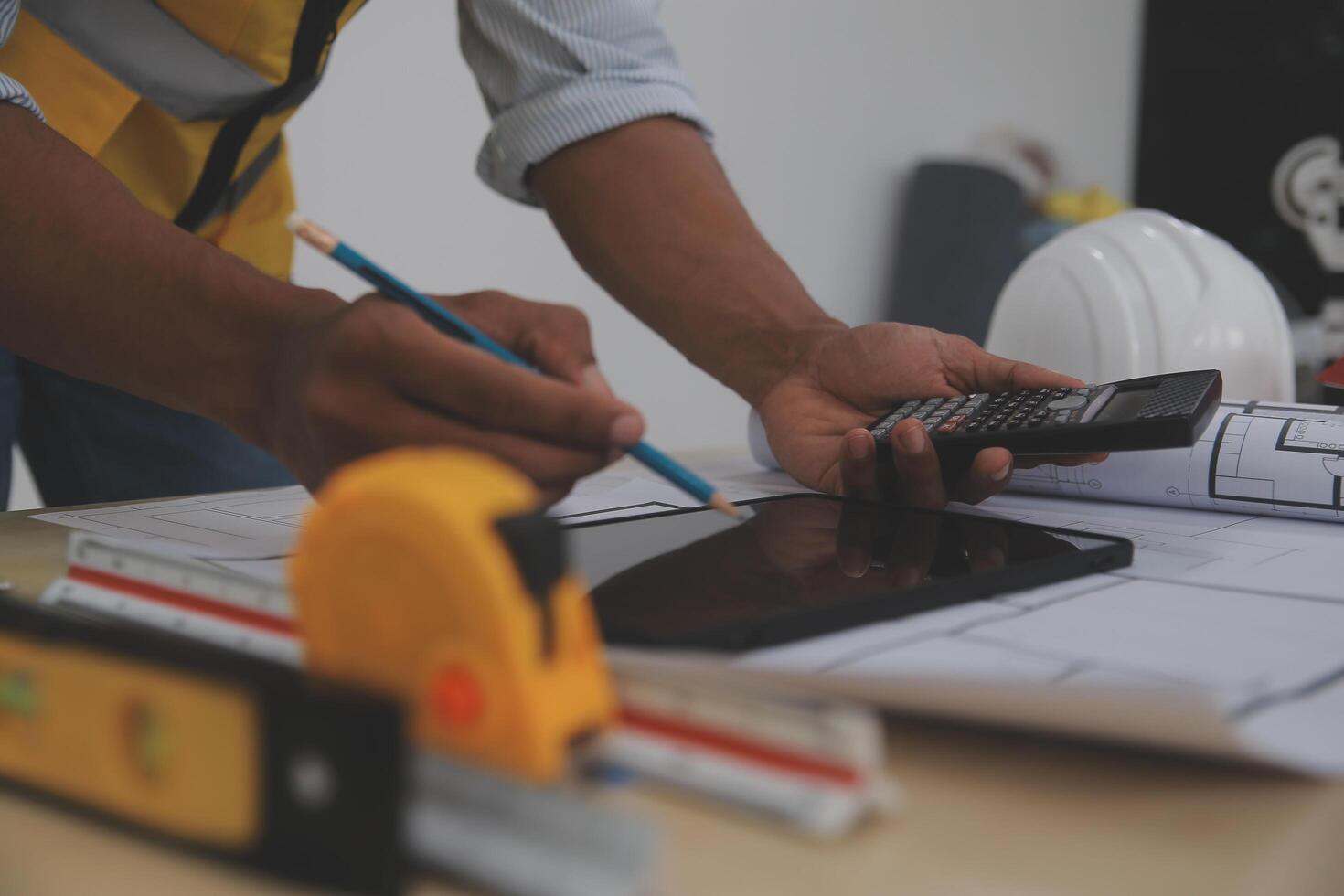 A man in a hard hat and safety vest is using a calculator and measuring tape photo