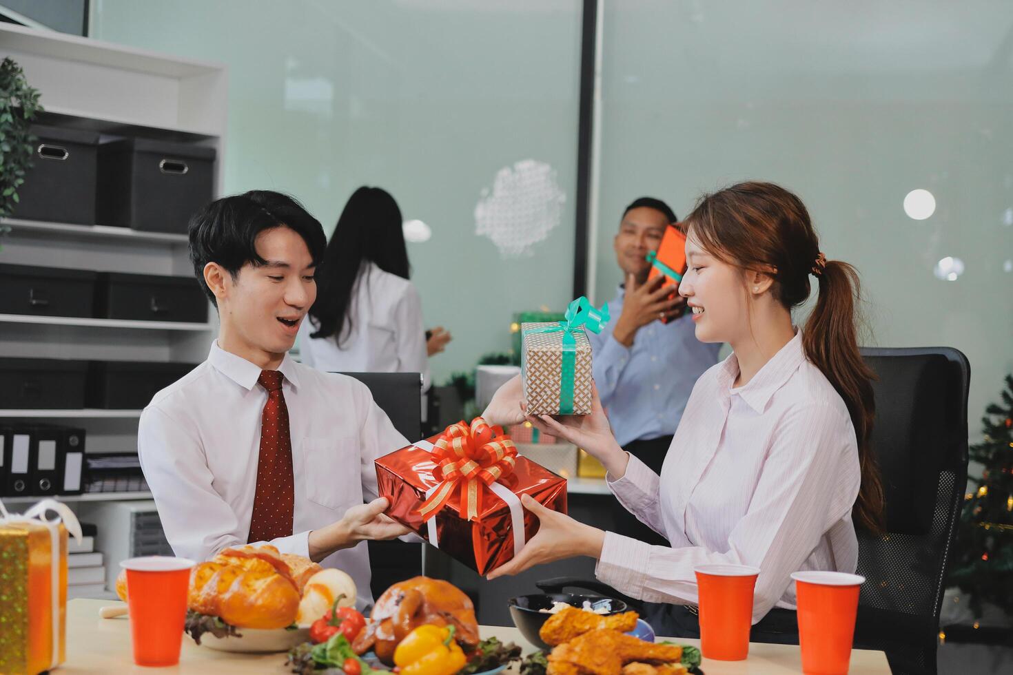 A man and woman are sitting at a table with a christmas tree and presents photo