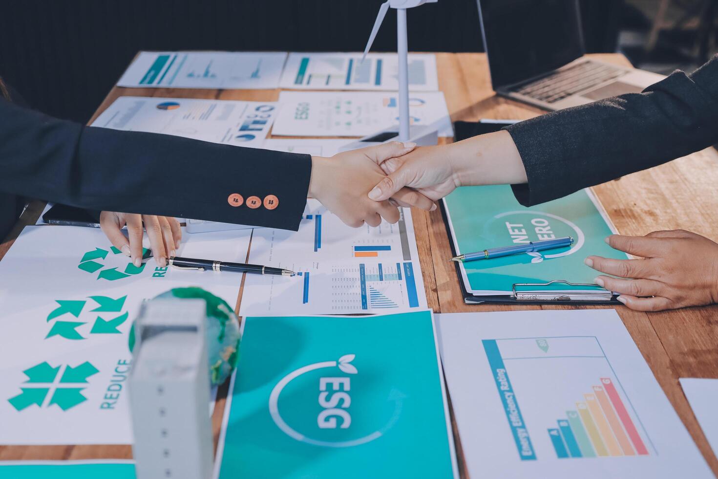 Business people shaking hands over a table with papers and other items photo