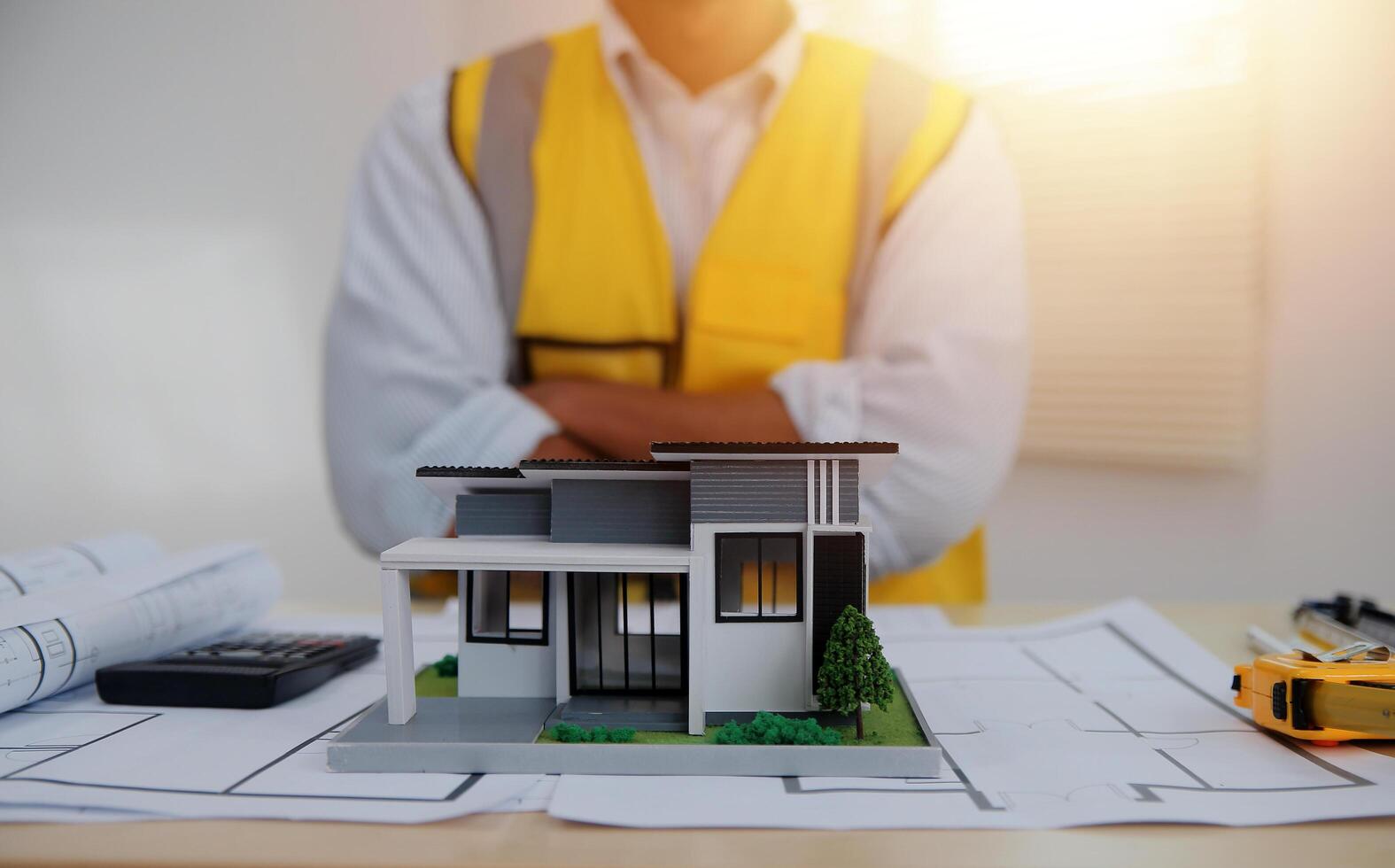 A man in a yellow vest and hard hat standing in front of a model house photo