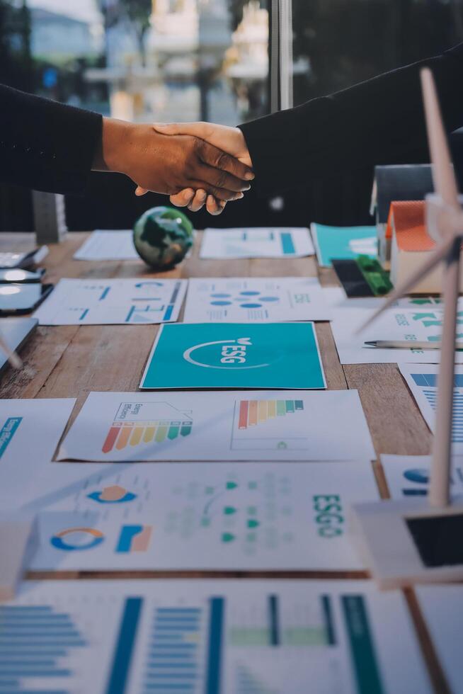 Two people shaking hands over a table with papers and graphs photo