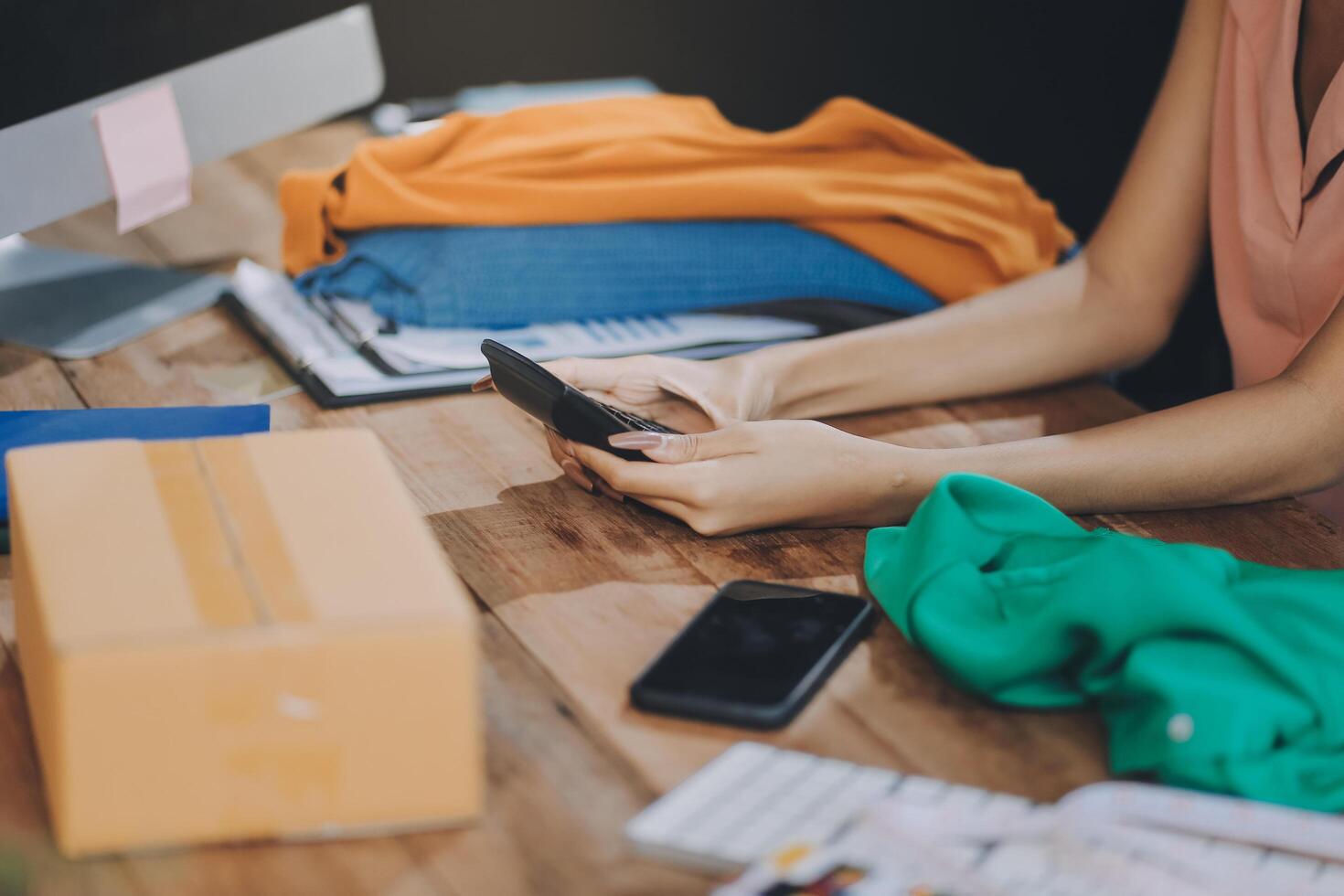 A woman is using her cell phone while sitting at a desk with a computer and other items photo