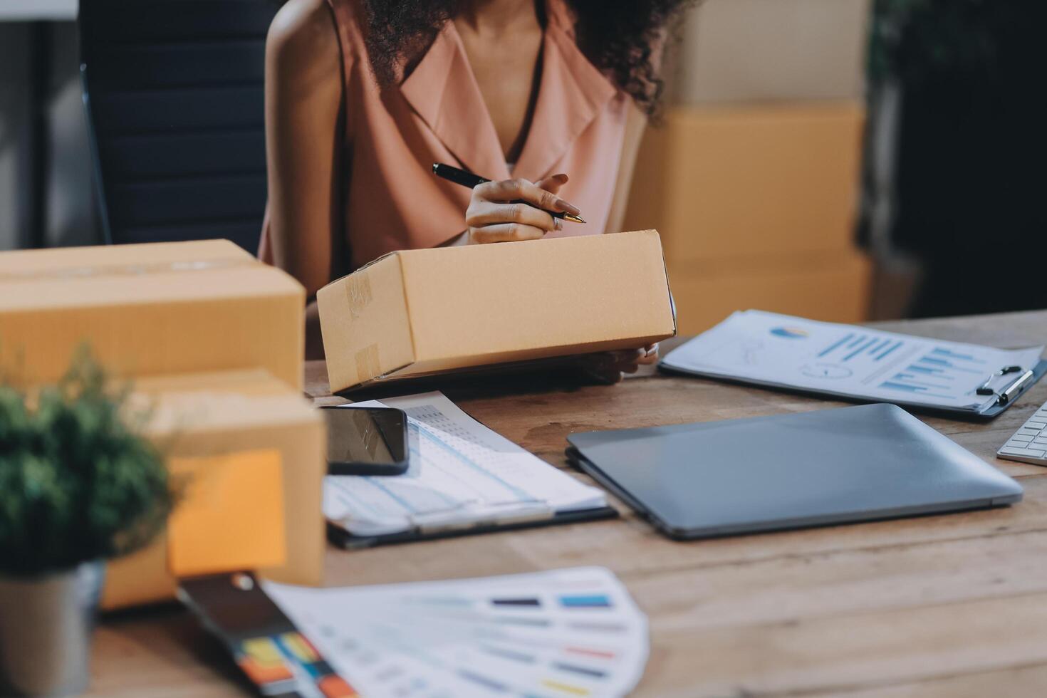 A woman is working on her laptop and holding a box photo
