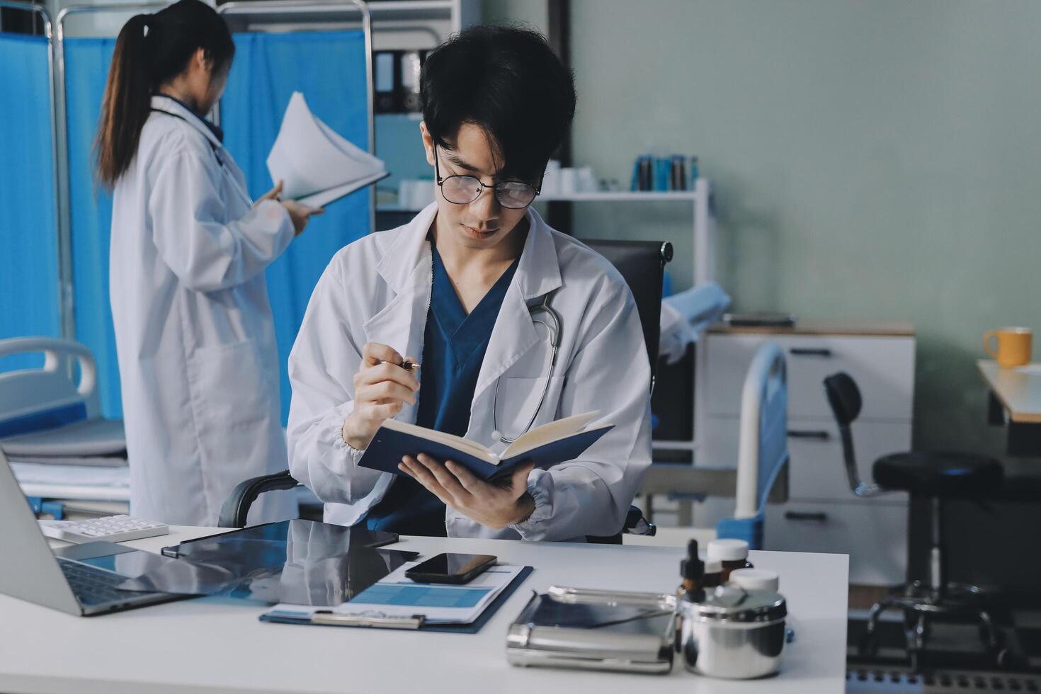 A doctor is writing on a book while another person is sitting at a desk photo