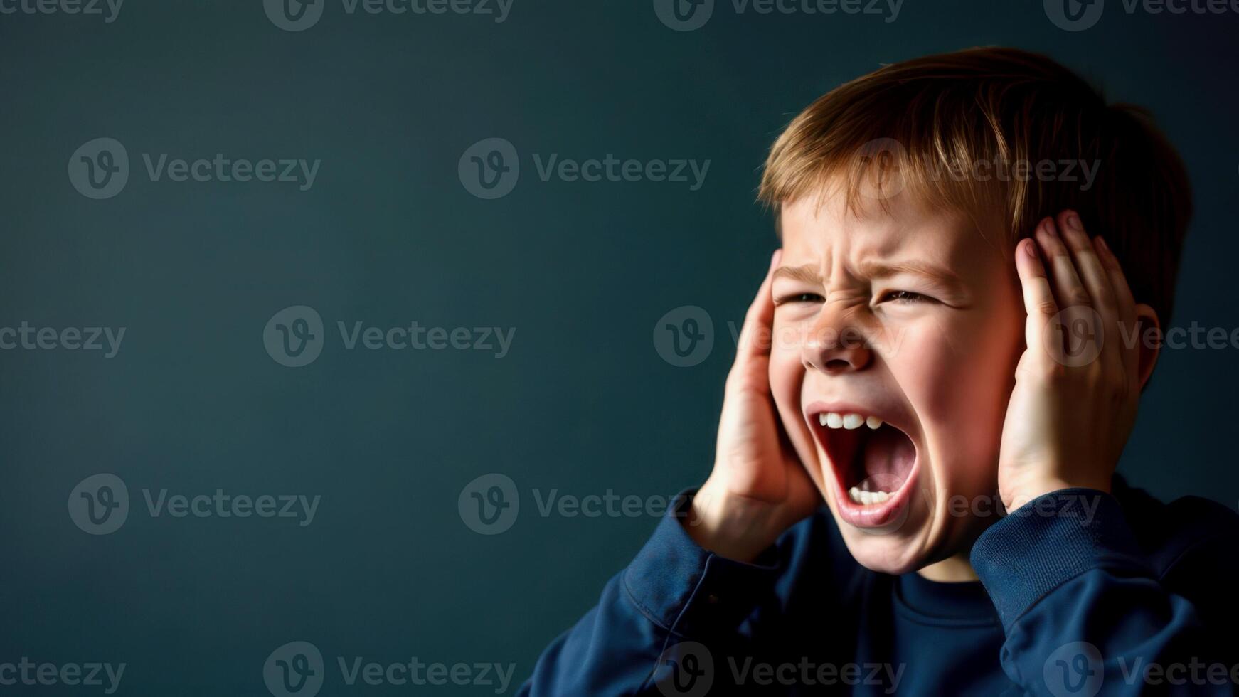 A portrait of a blond-haired boy screaming and covering his ears with both hands, on dark green background with empty space for text on the left, for banners, cards or messages photo