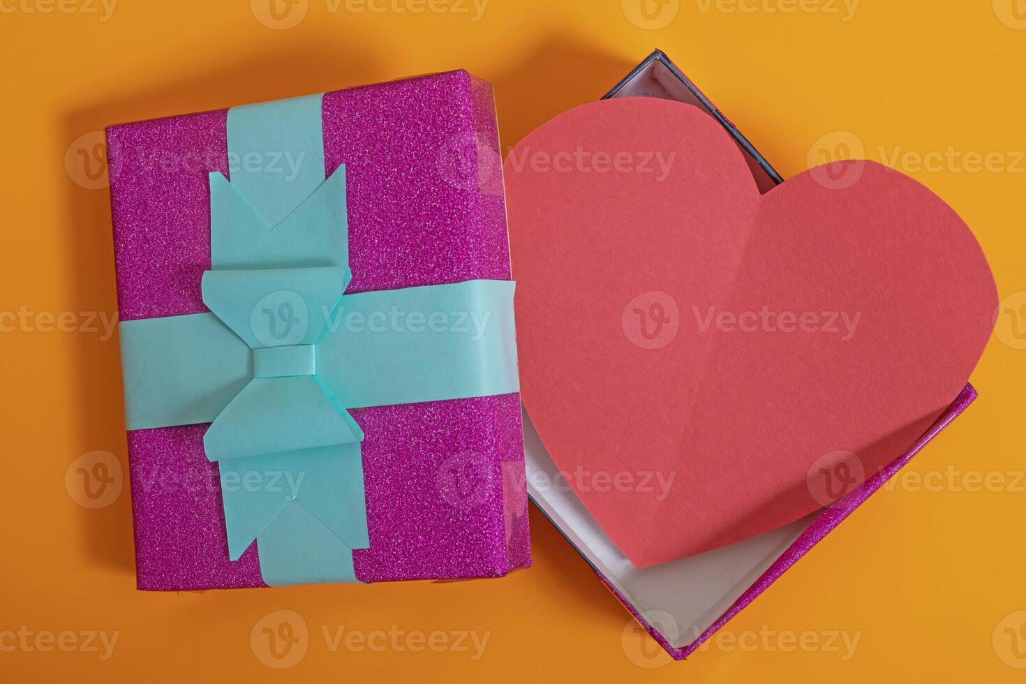 Top view of an open gift box with a red heart on a vibrant orange background for Valentine's Day and Mother's Day. photo
