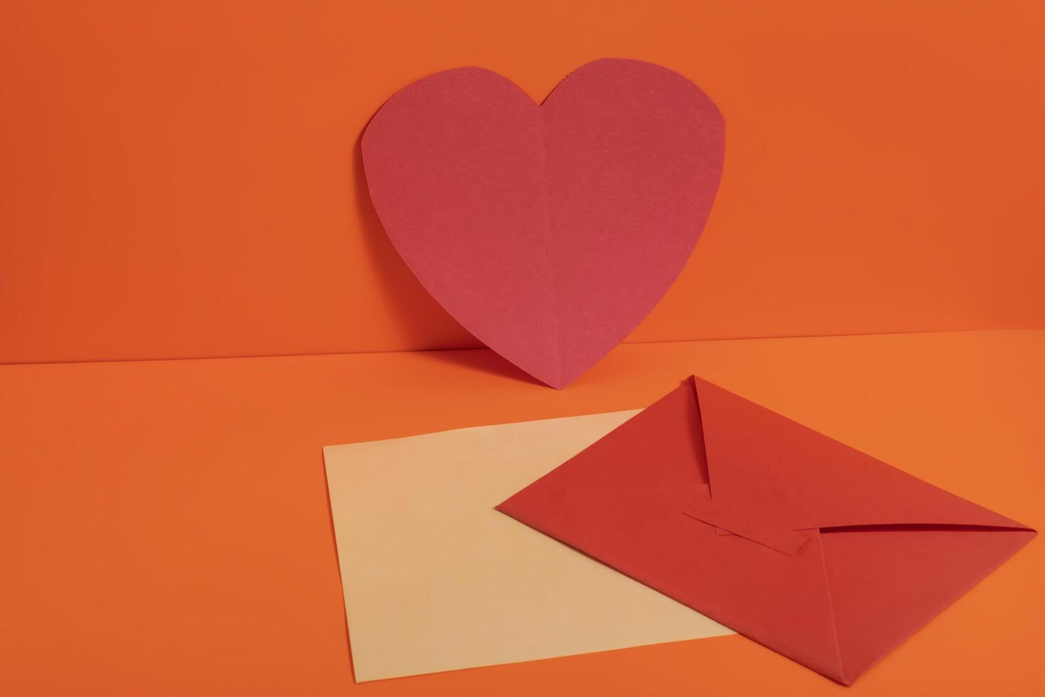 Red paper heart with envelopes on a vibrant orange background for Valentine's Day and Mother's Day. photo