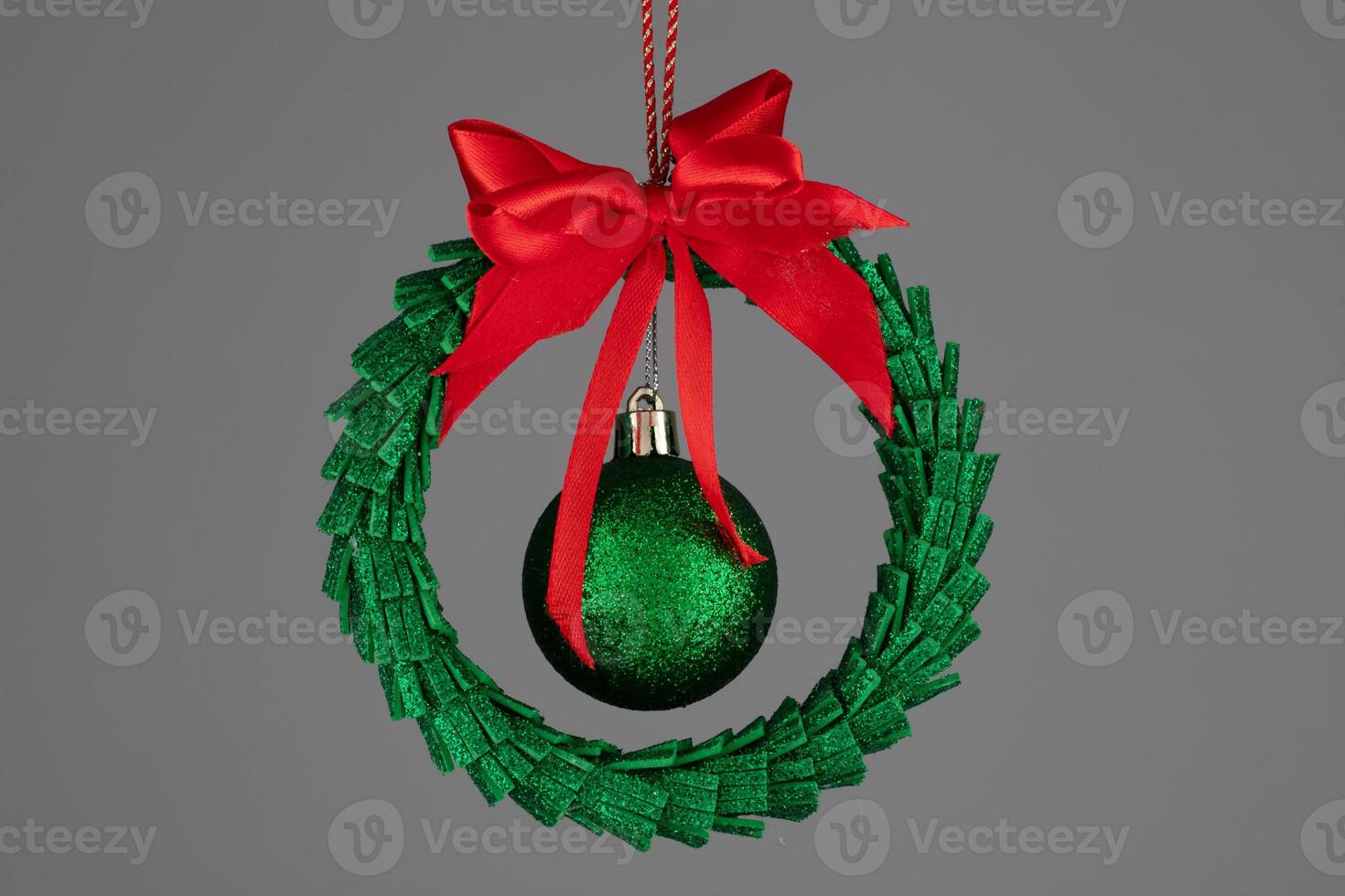 Green Christmas tree toy in the form of a garland with a ball and a red bow on a gray background. photo