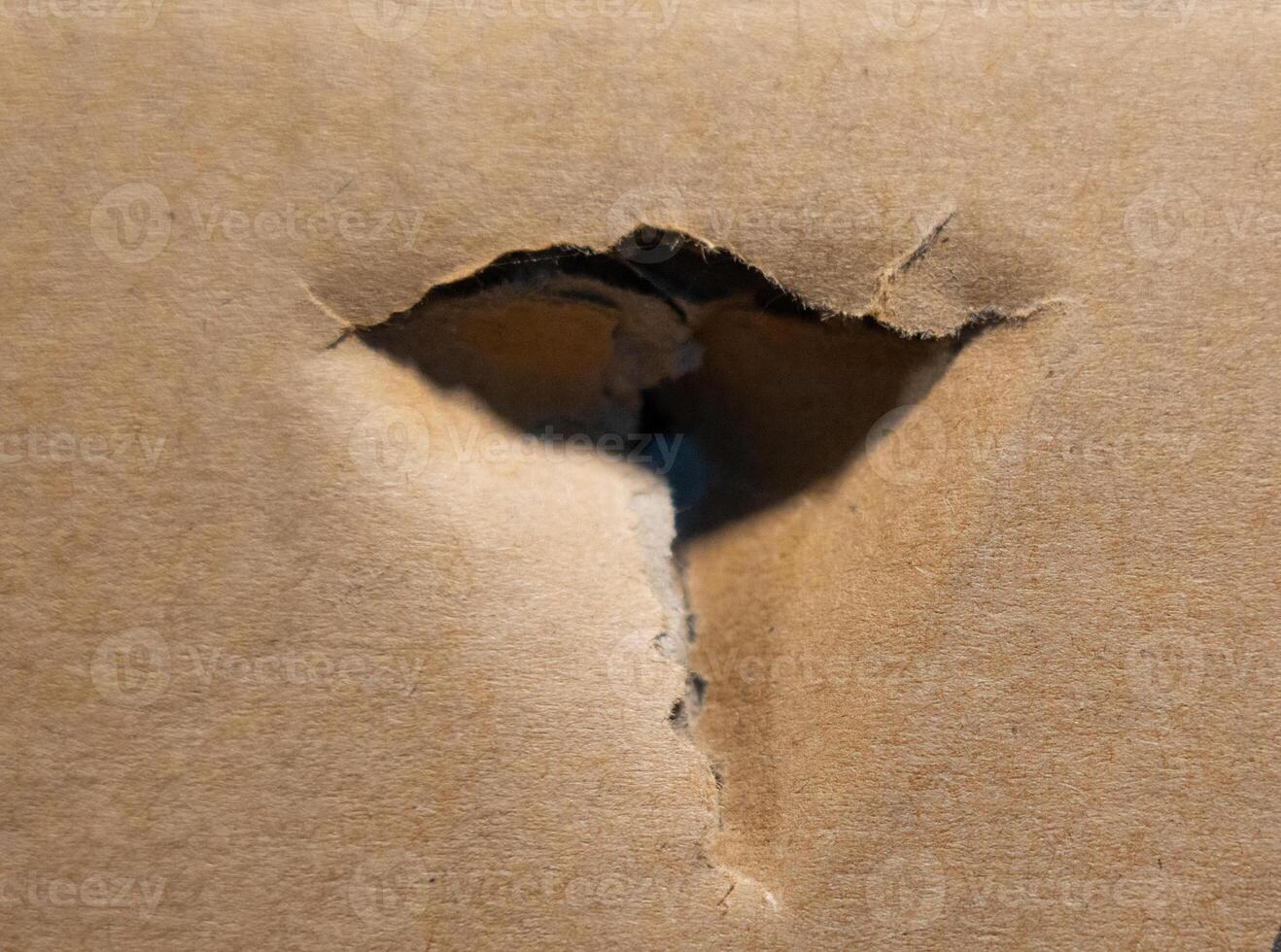 Torn hole in brown cardboard with rough edges photo