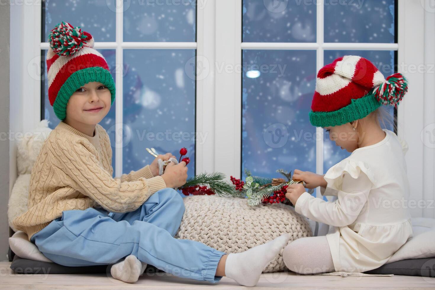 Little children brother and sister in Christmas hats play while sitting on a window photo