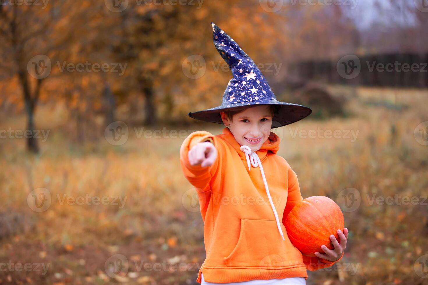 A child in an orange costume and a wizard hat for Halloween. A boy holds a pumpkin on an autumn background. A child at a Halloween party. photo