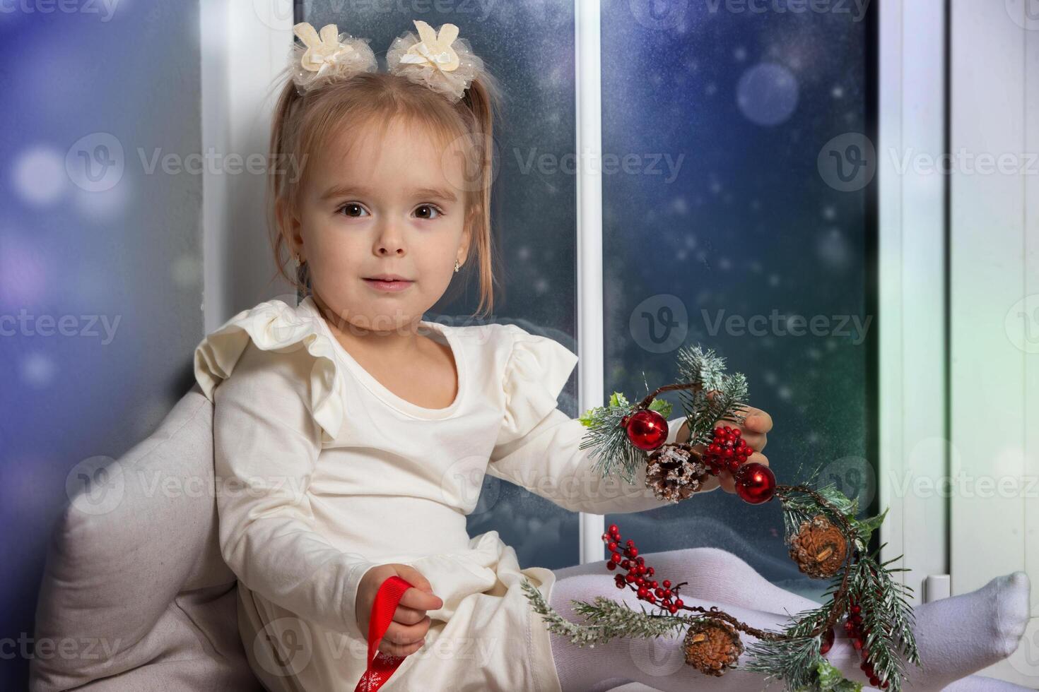 Little happy girl sitting on the windowsill playing with Christmas decor photo
