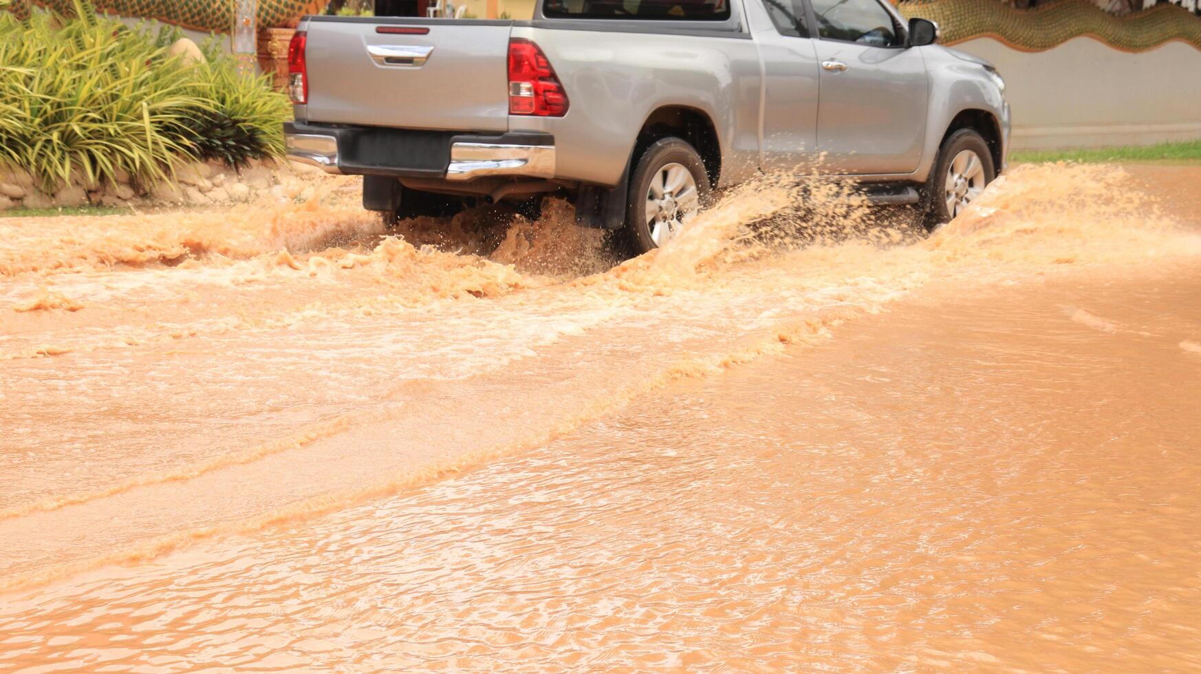 A vehicle navigates through muddy floodwater depicting urban resilience and the impact of heavy rain. This image highlights extreme weather, climate change, and transportation challenges. photo