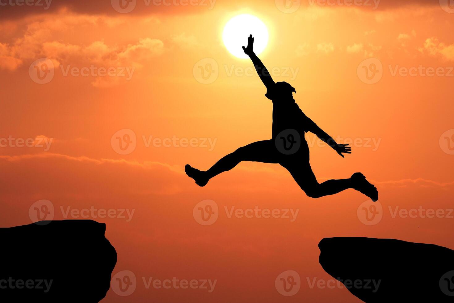 Silhouette of Person Leaping Across Gap with Vibrant Sunset Sky and Sun in Background Symbolizing Courage and Achievement photo