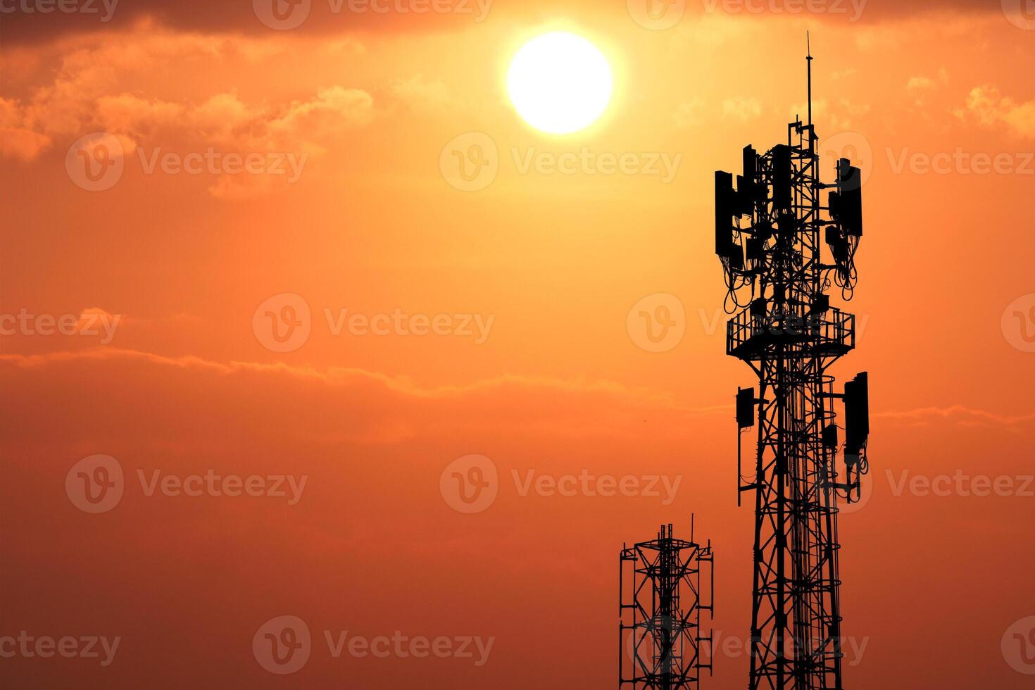 Silhouetted Communication Towers Against a Vibrant Orange Sunset Sky with Glowing Sun and Cloudy Horizon photo