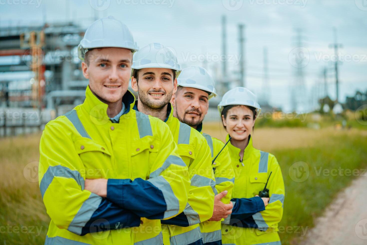 Four construction workers pose confidently at a power plant site during daylight, showcasing teamwork and safety gear photo