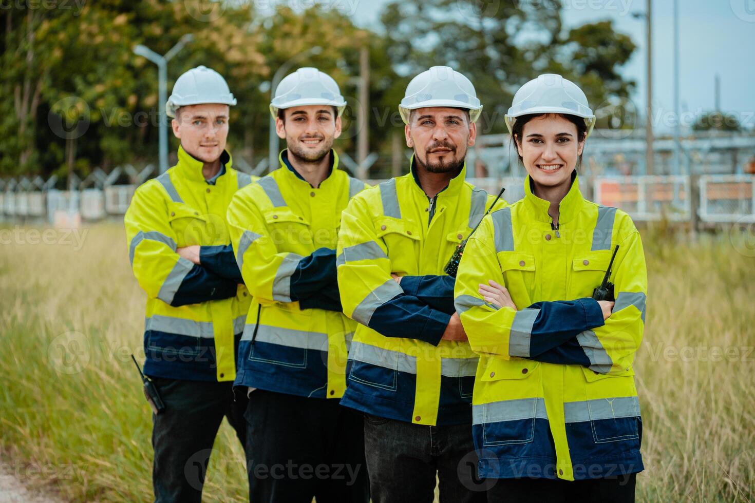 Group of construction workers in safety gear standing confidently in a grassy area near a work site during daylight photo