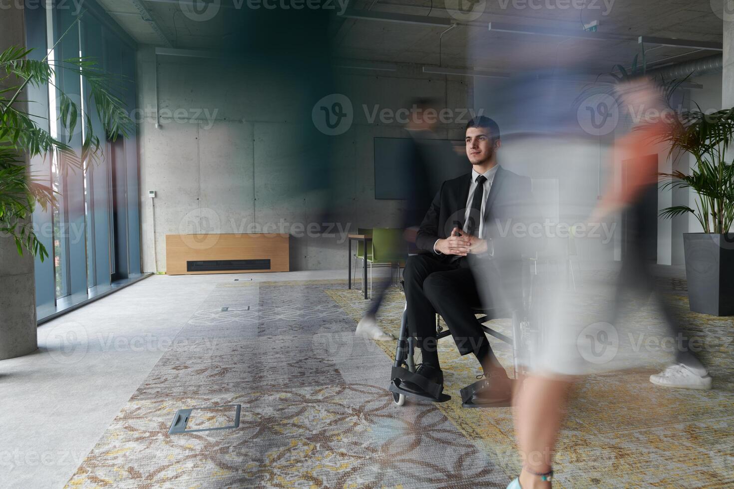 A businessman in a wheelchair navigating through a busy office, surrounded by his colleagues who are actively engaged in their work and collaboration photo