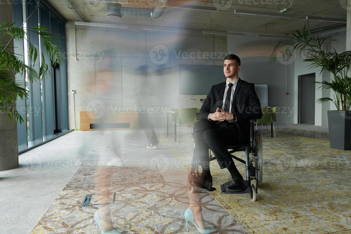 A businessman in a wheelchair navigating through a busy office, surrounded by his colleagues who are actively engaged in their work and collaboration photo