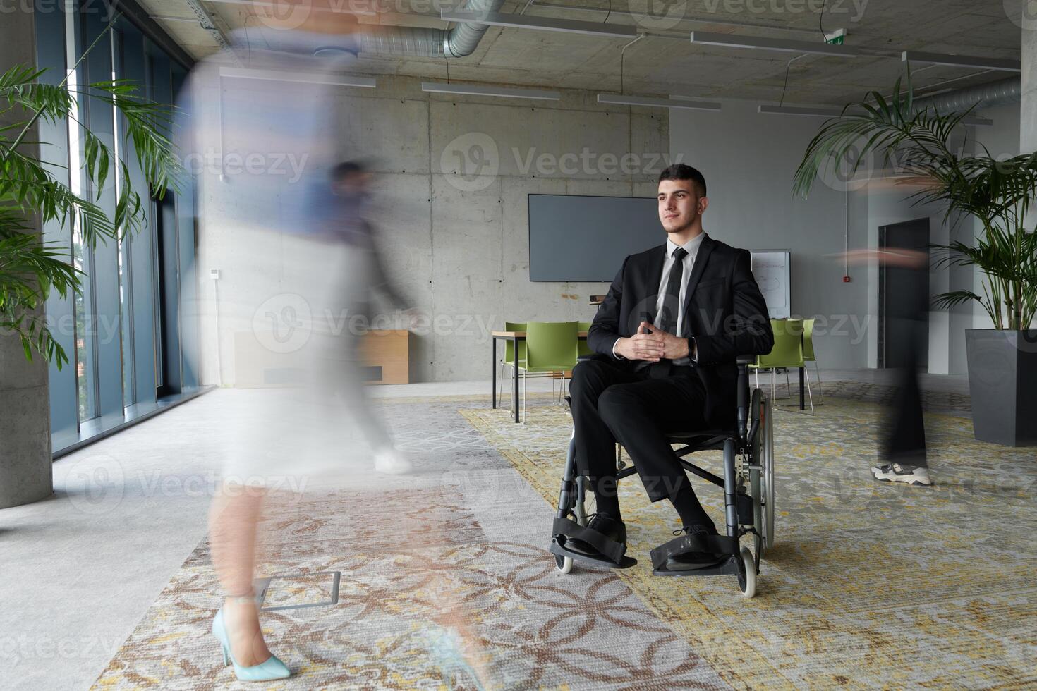 A businessman in a wheelchair navigating through a busy office, surrounded by his colleagues who are actively engaged in their work and collaboration photo