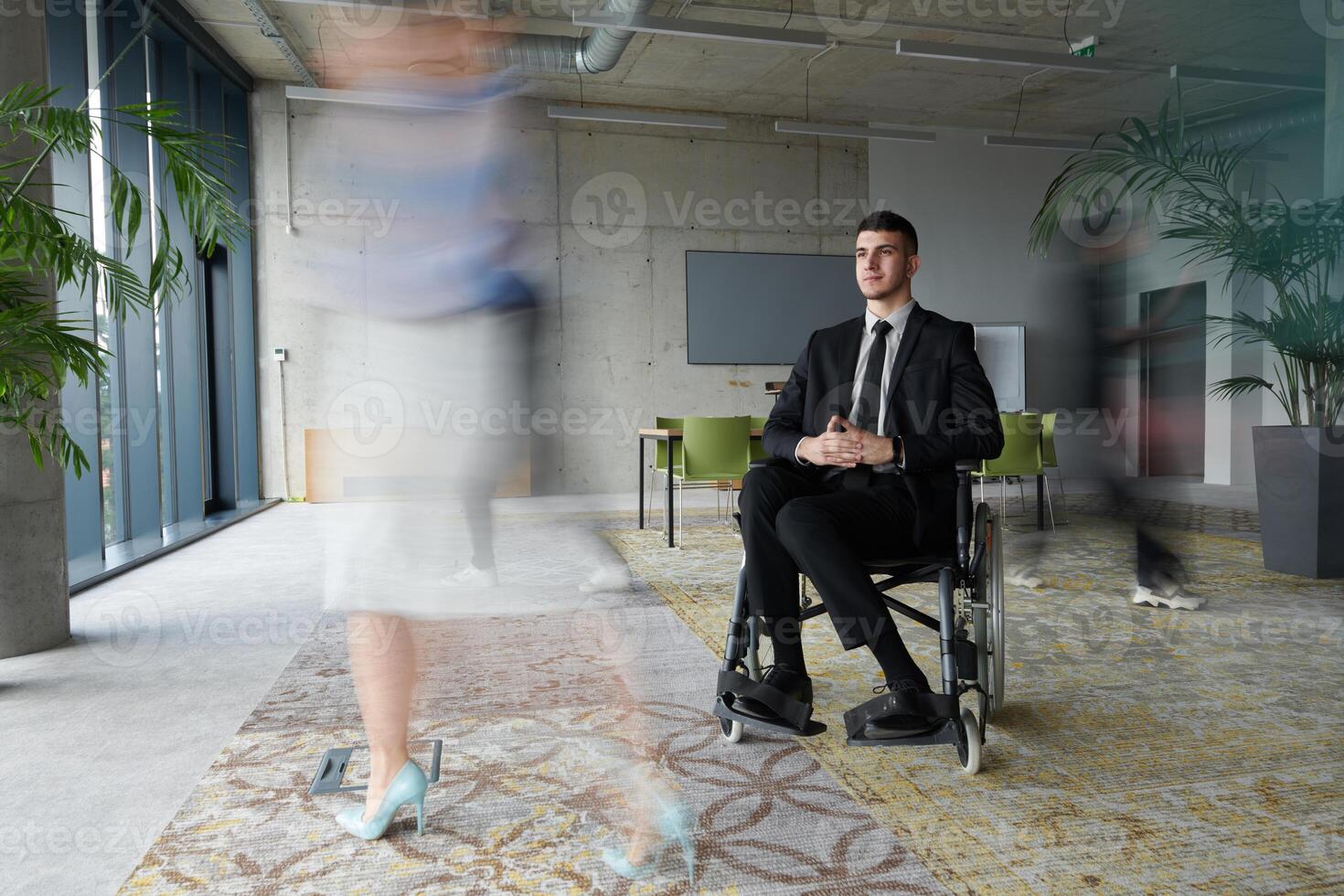 A businessman in a wheelchair navigating through a busy office, surrounded by his colleagues who are actively engaged in their work and collaboration photo