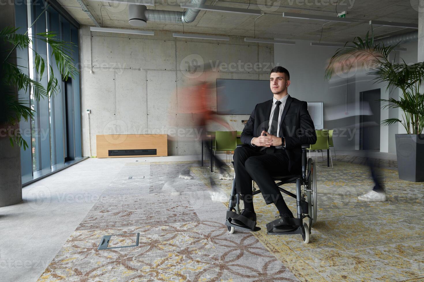 A businessman in a wheelchair navigating through a busy office, surrounded by his colleagues who are actively engaged in their work and collaboration photo