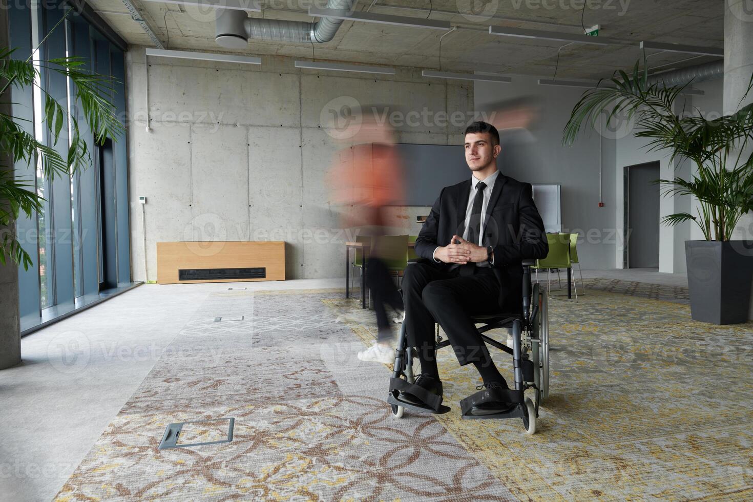 A businessman in a wheelchair navigating through a busy office, surrounded by his colleagues who are actively engaged in their work and collaboration photo