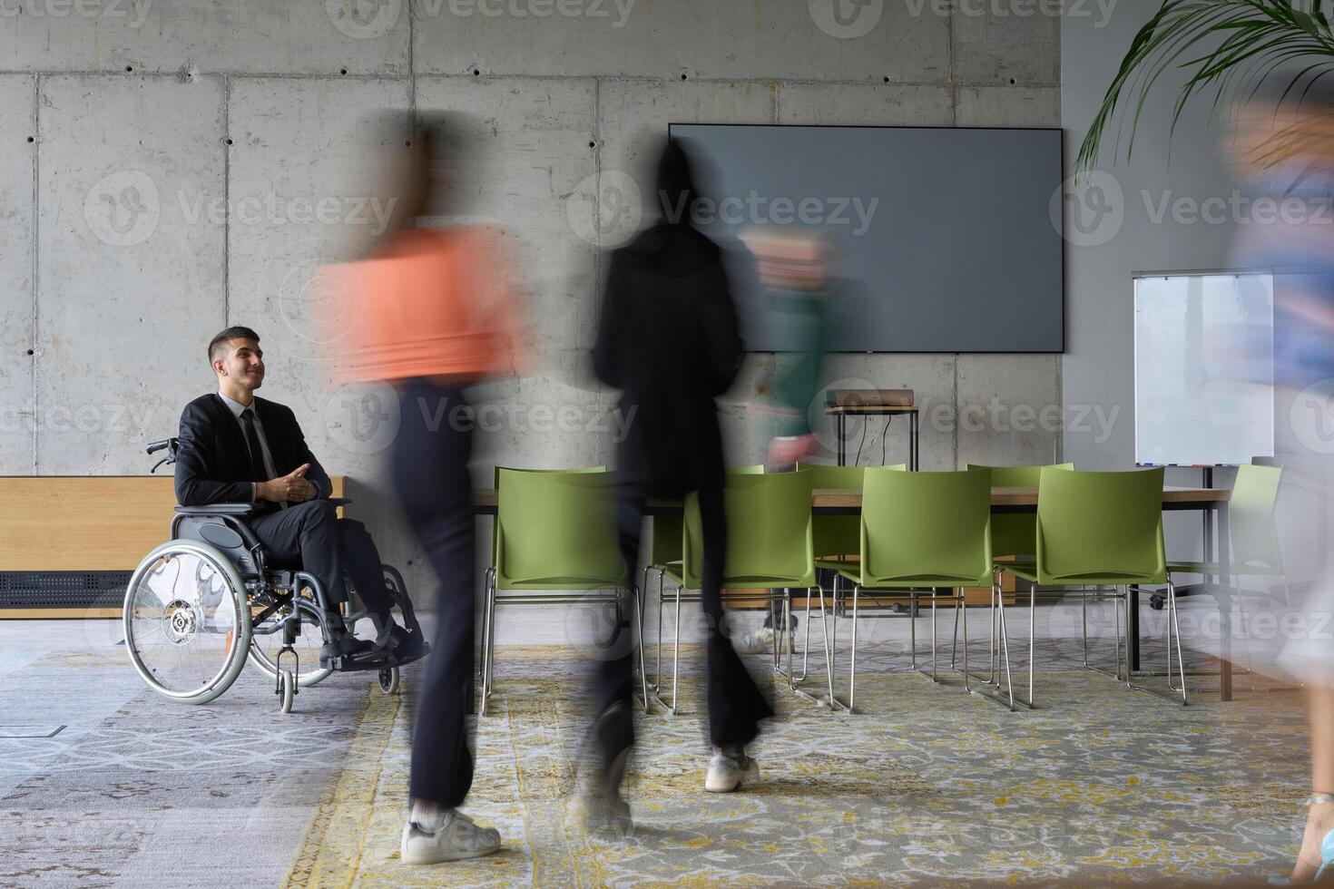 A diverse business team, working urgently around a conference table, collaborates on a meeting while their director, seated in a wheelchair, waits for their input photo