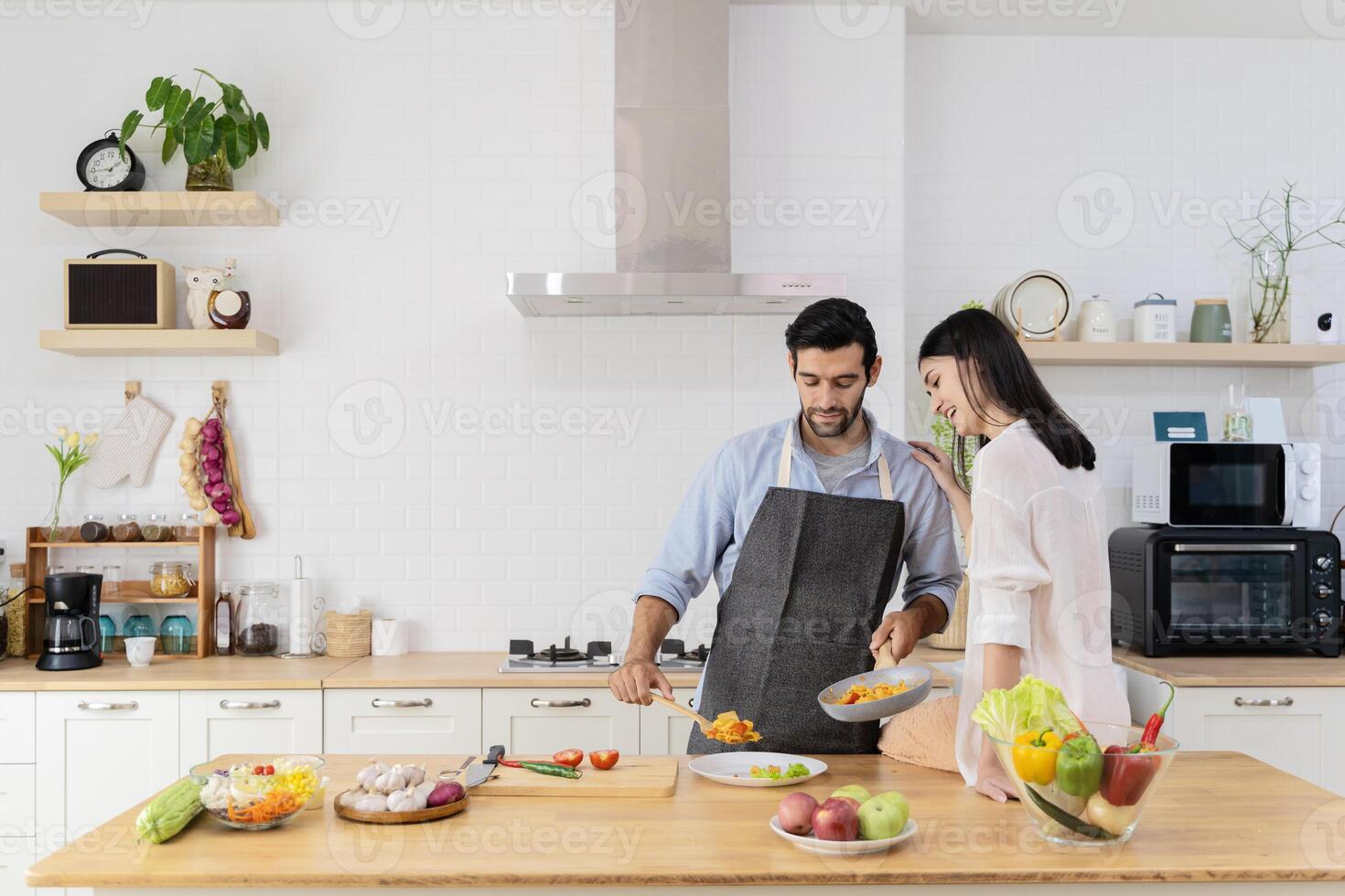 Pretty young couple in the kitchen, family of two preparing food, woman sitting on kitchen table and helping man photo