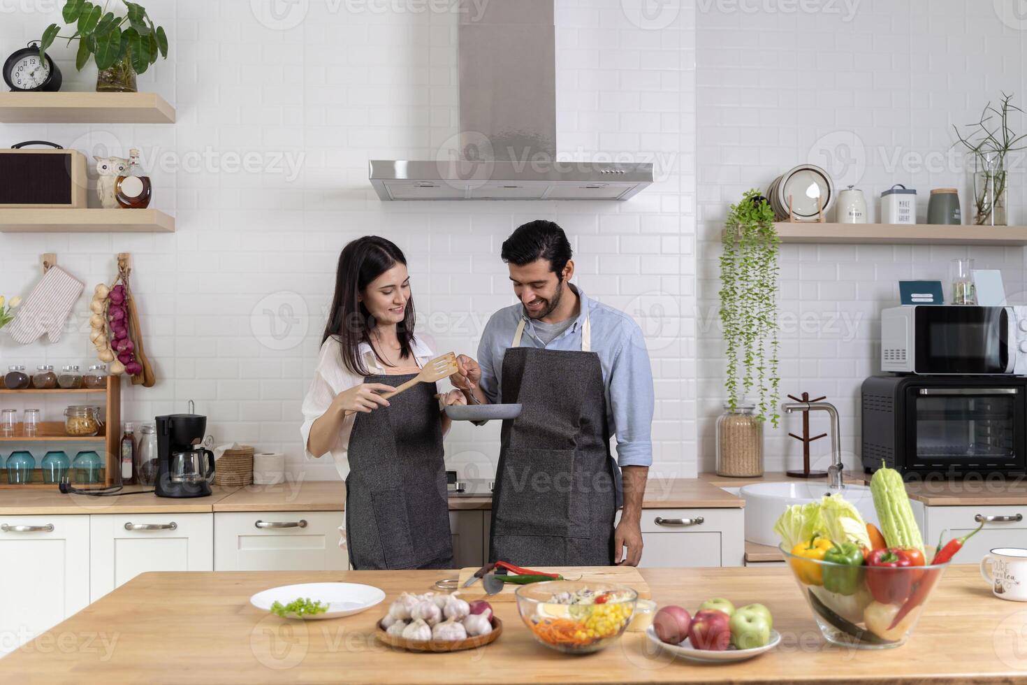 Romantic couple is cooking in the kitchen. A handsome man and a charming young woman are having fun together while making salad. photo