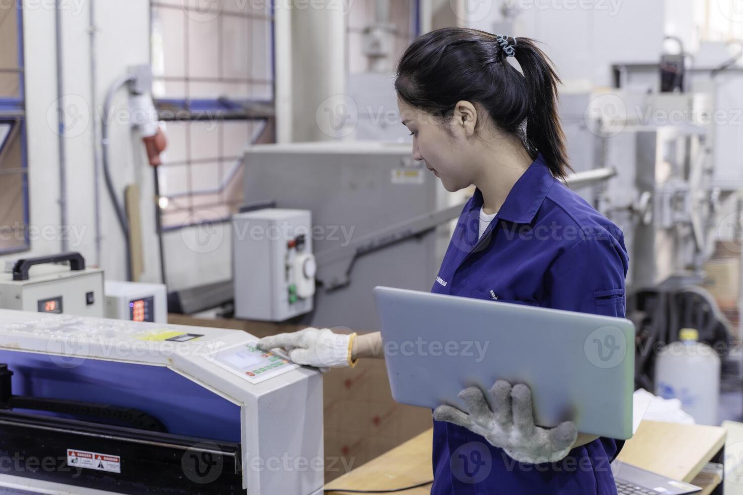 Asian woman industrial engineer wearing uniform using laptop checking automated machine in industrial workshop. photo