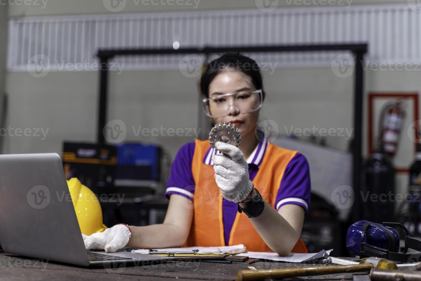 Asian woman technician engineer working designing mechanical parts engineering with laptop and example small gear in hand at industrial workshop. photo
