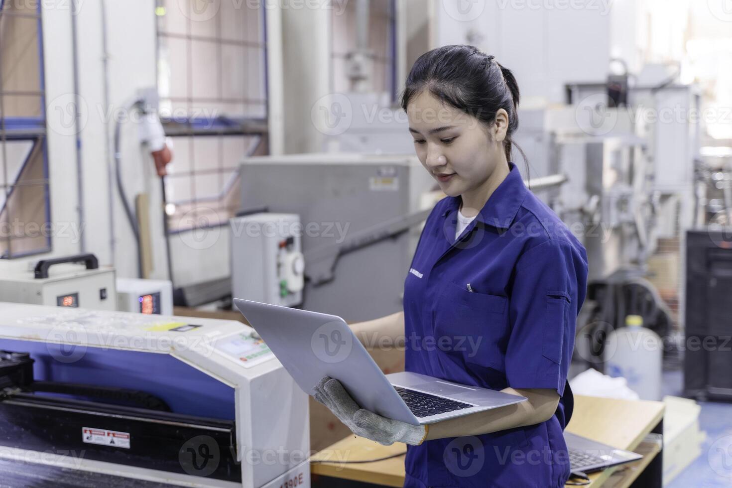 Asian woman industrial engineer wearing uniform using laptop control automated machine in industrial photo